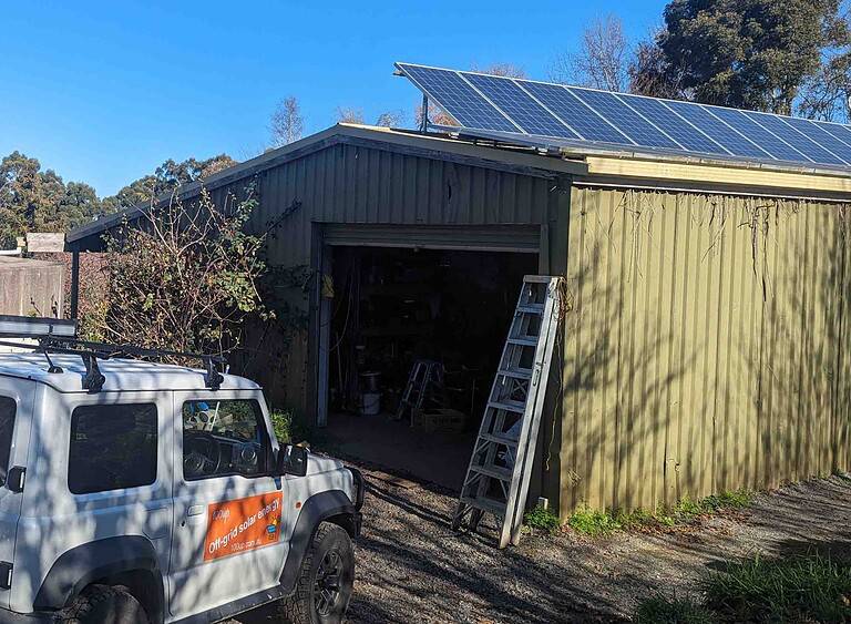 Solar panels installed on corrugated iron shed roof with Off Grid Solar Energy installer vehicle and ladder visible