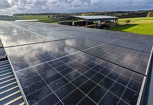 Extensive solar panel installation on rural property roof with rolling hills and cloudy sky in background