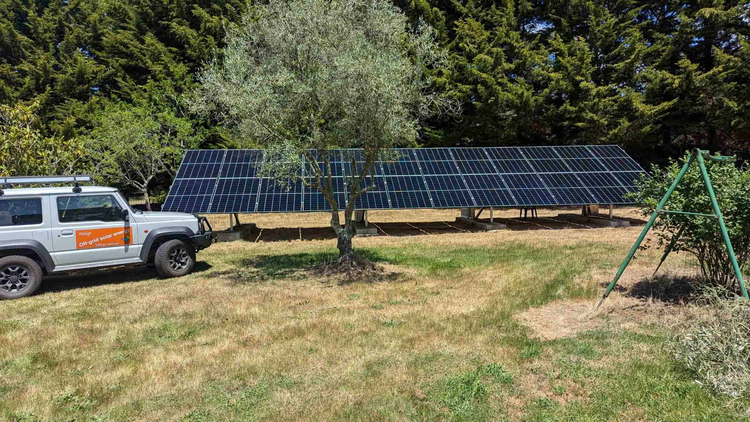 Large ground-mounted solar panel array with 100up service vehicle on rural Victorian property with trees in background