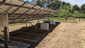 Ground-mounted solar panel array with inverter boxes on concrete pads beneath the panels in rural setting