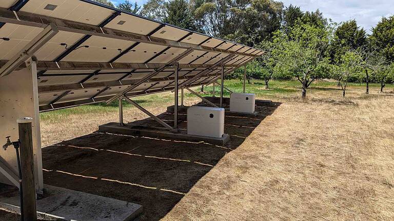 Ground-mounted solar panel array with inverter boxes on concrete pads beneath the panels in rural setting