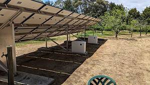 Ground-mounted solar panel array with metal frame structure and two white Pylontech battery cabinets underneath in Ballarat