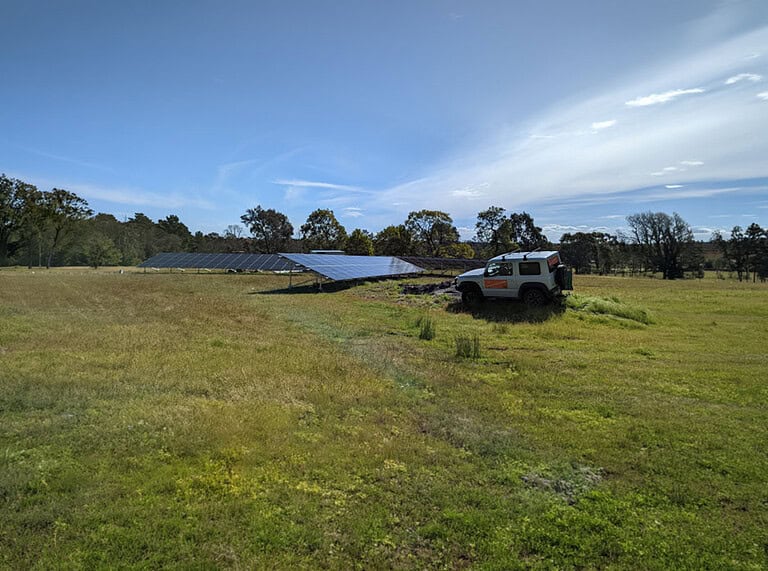 Large ground-mounted solar panel installation in rural field with 100up service vehicle parked nearby under blue sky