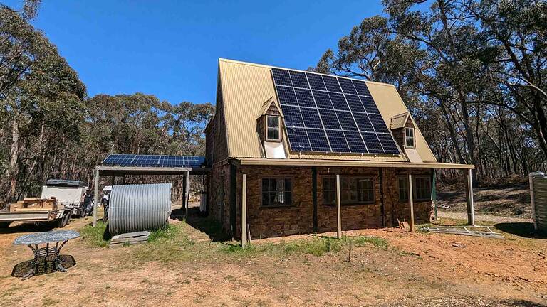 Stone and timber home with solar panels covering most of the metal roof, surrounded by bushland in regional Victoria