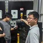 Three technicians installing and configuring off-grid solar inverters and control systems in an industrial facility