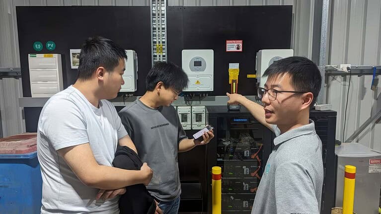 Three technicians installing and configuring off-grid solar inverters and control systems in an industrial facility