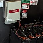 Black lithium battery modules with red DC cables and warning signs including restricted access and toxic fumes notices