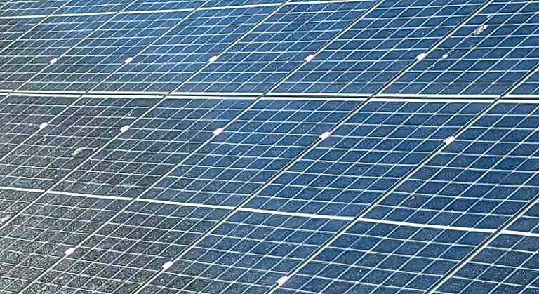 Large solar panel installation showing multiple rows of photovoltaic panels with visible mounting frames and connections