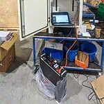 White electrical cabinet with door open showing inverters and control equipment, laptop connected for testing in warehouse