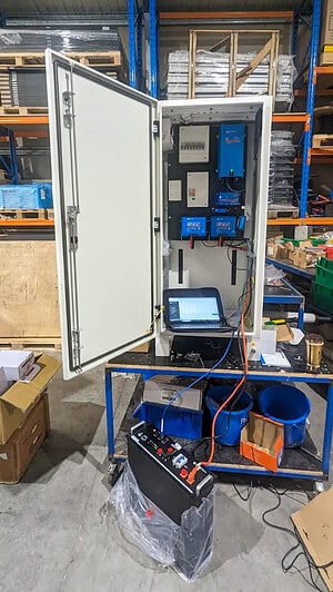 White electrical cabinet with door open showing inverters and control equipment, laptop connected for testing in warehouse