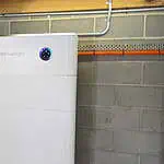 White SidEnergy battery unit mounted on basement wall with blue LED indicators showing system status