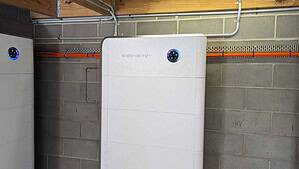 White SidEnergy battery unit mounted on basement wall with blue LED indicators showing system status
