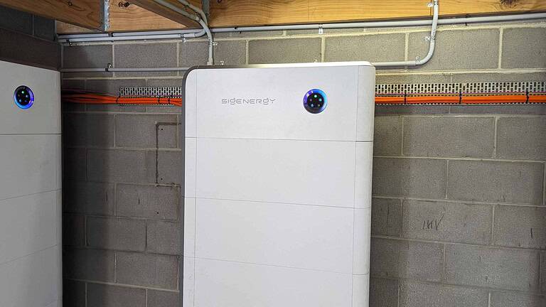 White SidEnergy battery unit mounted on basement wall with blue LED indicators showing system status