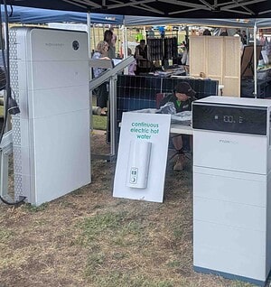 Solar equipment display under tent showing Pylontech battery system, air conditioning unit, and continuous electric hot water setup