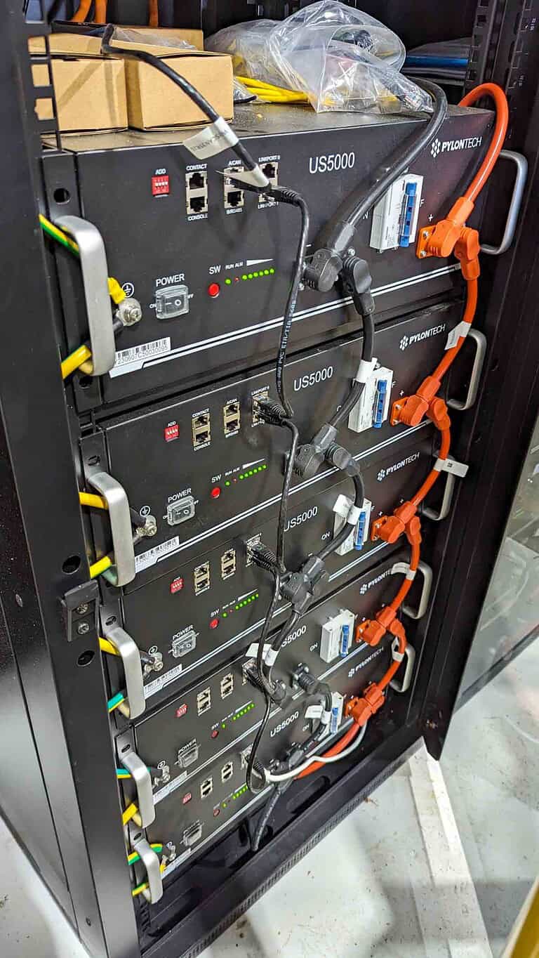 Four Pylontech US5000 lithium batteries mounted in server rack with orange high-voltage DC cables and management systems