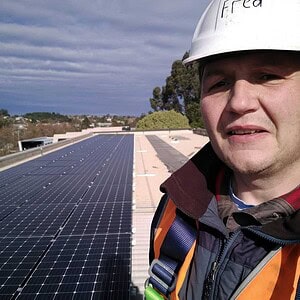 Solar technician in safety gear standing on large commercial rooftop solar panel installation in Ballarat