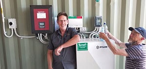 Technicians standing beside off grid solar battery system and inverter setup inside utility container