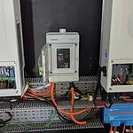 Two white Deye inverters with digital displays mounted above electrical switchboard with orange and black cables