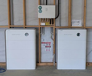 Two white SIGenergy battery units installed in unfinished building with electrical connections and safety warning labels