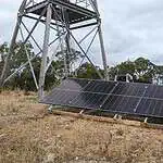 Ground-mounted solar panel array installed near telecommunications tower in rural Australian bushland setting