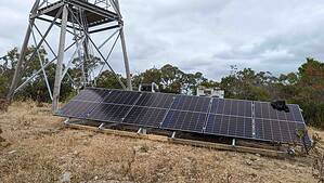 Ground-mounted solar panel array installed near telecommunications tower in rural Australian bushland setting