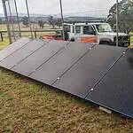 Ground-mounted solar panel array with white battery storage unit behind security fencing in rural Victorian setting