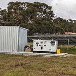 Off-grid solar installation with metal shed, Hyundai backup generator, and solar panel arrays in rural setting