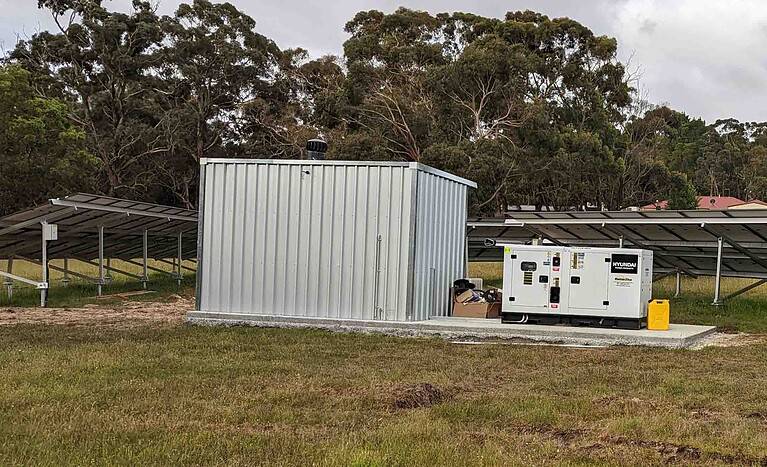 Off-grid solar installation with metal shed, Hyundai backup generator, and solar panel arrays in rural setting