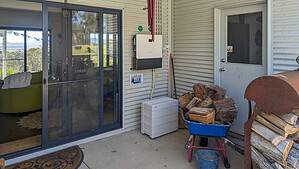 Off-grid solar system components including inverter, battery storage, and firewood pile on covered outdoor area in Queensland