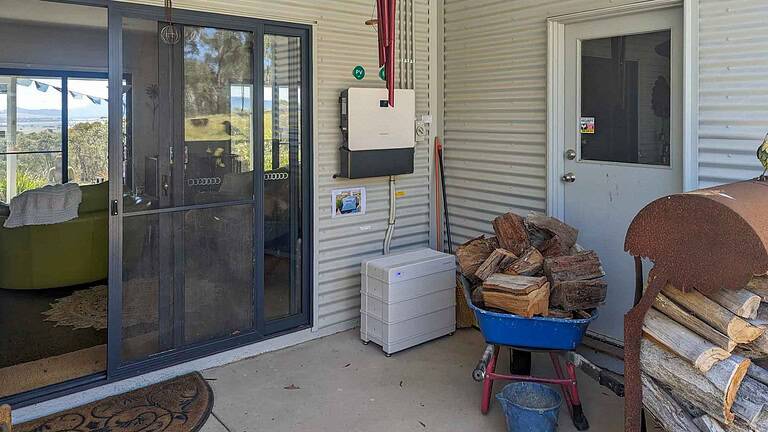 Off-grid solar system components including inverter, battery storage, and firewood pile on covered outdoor area in Queensland