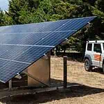 Large ground-mounted solar panel array on concrete foundations in rural setting with vehicle parked nearby
