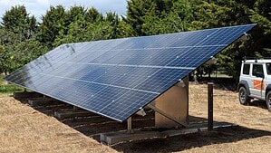 Large ground-mounted solar panel array on concrete foundations in rural setting with vehicle parked nearby