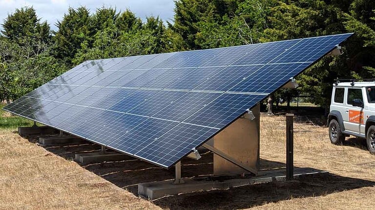 Large ground-mounted solar panel array on concrete foundations in rural setting with vehicle parked nearby