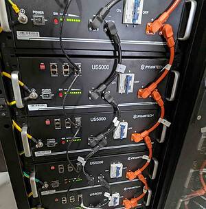 Stack of five Pylontech US5000 lithium batteries in server rack with orange DC cables and monitoring connections