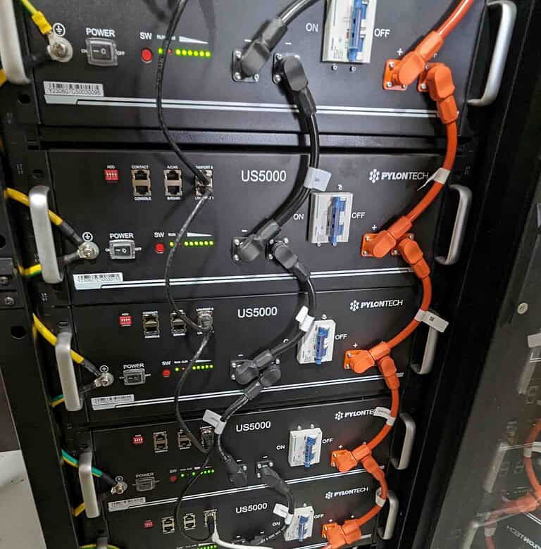 Stack of five Pylontech US5000 lithium batteries in server rack with orange DC cables and monitoring connections