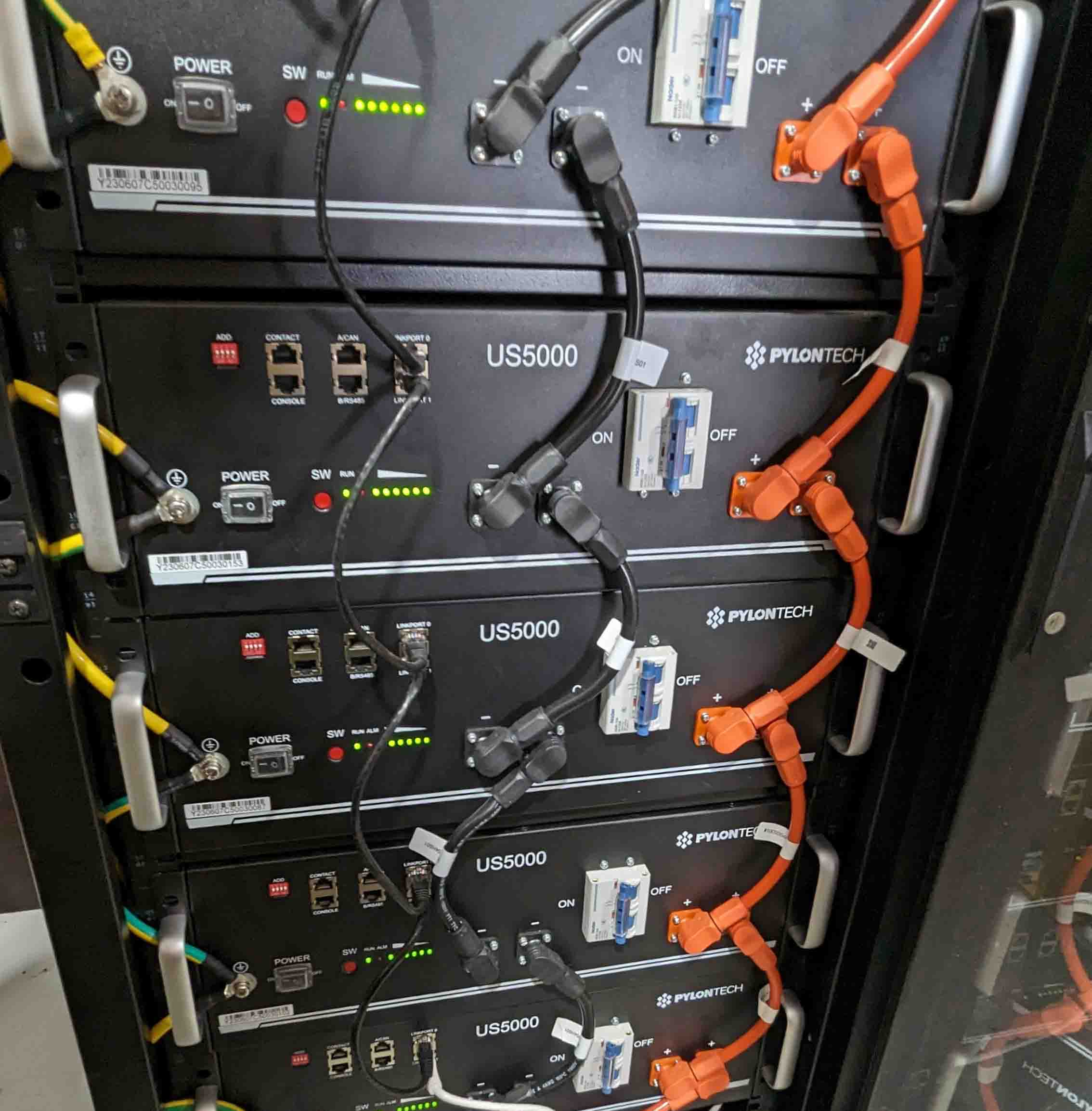 Stack of five Pylontech US5000 lithium batteries in server rack with orange DC cables and monitoring connections