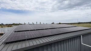 Solar panels mounted on corrugated metal roof of building in rural Victoria with cloudy sky and farmland background