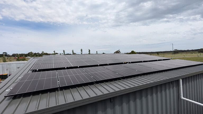 Solar panels mounted on corrugated metal roof of building in rural Victoria with cloudy sky and farmland background