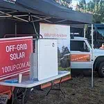 100UP off-grid solar display trailer with signage and solar equipment at outdoor community event under marquee tent