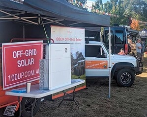 100UP off-grid solar display trailer with signage and solar equipment at outdoor community event under marquee tent