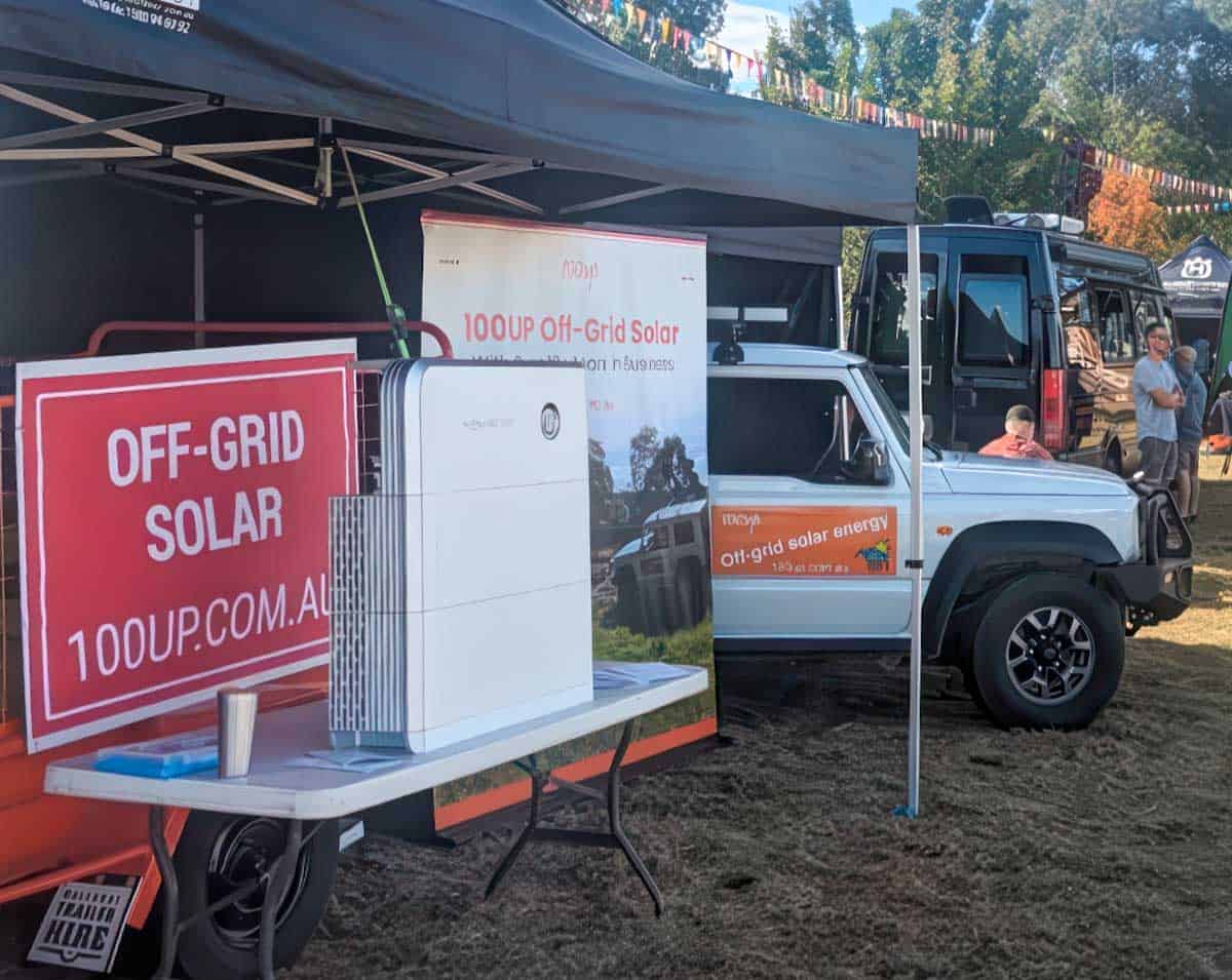 100UP off-grid solar display trailer with signage and solar equipment at outdoor community event under marquee tent