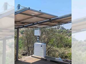 White Enphase battery unit mounted under solar panel canopy structure with hills and vegetation in background