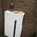 White AlphaESS battery storage units stacked against brick wall with red drill and tools on top during installation