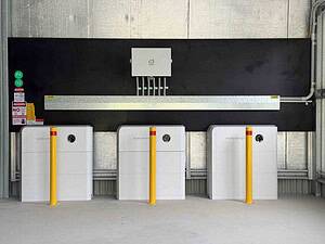 Three white Sigenergy battery units with yellow safety bollards installed in warehouse for 48 kWh off-grid system in Kempsey NSW