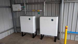 Two white Sigenergy 6kW inverters mounted on black stands in an industrial shed, providing 12kW combined power output