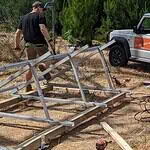 Off-grid solar installer assembling aluminium ground mount frame with tools and equipment scattered on cleared ground