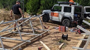 Off-grid solar installer assembling aluminium ground mount frame with tools and equipment scattered on cleared ground