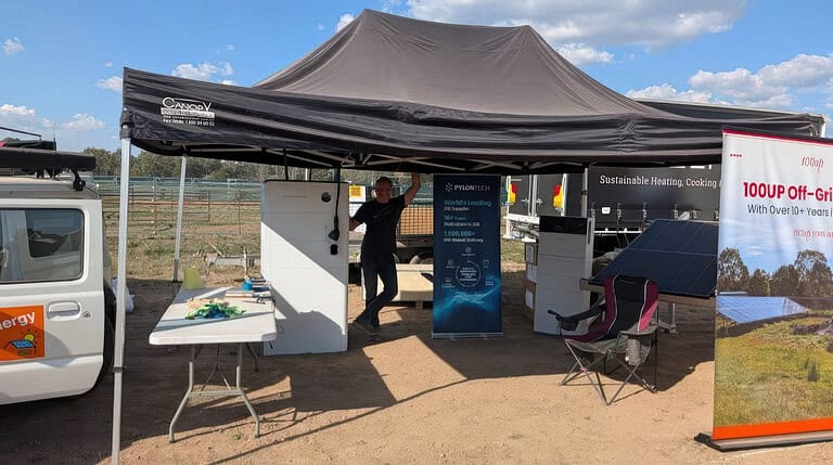 Portable solar display booth with gazebo, demonstration table, battery system banners and promotional materials in rural field