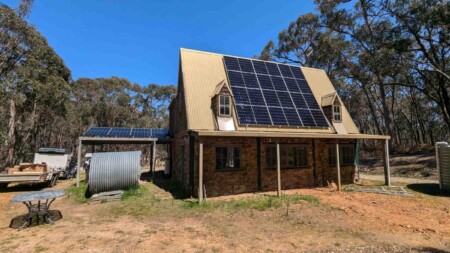 Stone and timber home with solar panels covering most of the metal roof, surrounded by bushland in regional Victoria