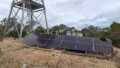 Ground-mounted solar panel array installed near telecommunications tower in rural Australian bushland setting